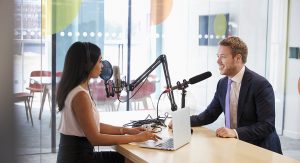 A woman interviewing a man for a podcast in a contemporary and branded office setting.