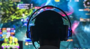 Silhouette of a video game plater wearing headphones with an out-of-focus video game screed in the background.
