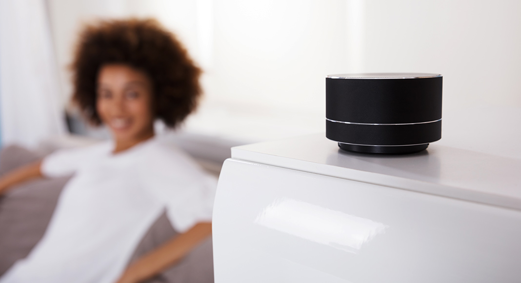 an Amazon Smart Speaker sitting on an end table next to a woman who looks pleased to own the smart speaker.