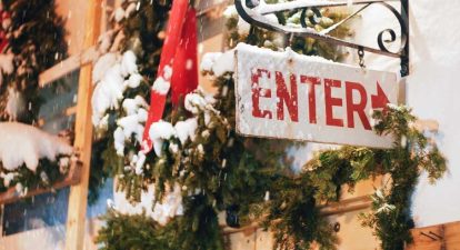 An enter sign dusted with snow against a background of pine boughs and holiday decor.