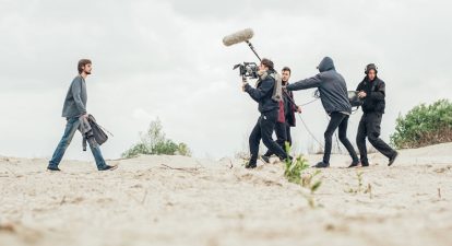 A lead actor being filmed by a crew on an outdoor set.