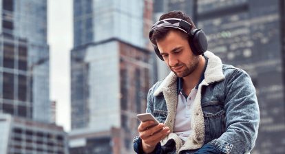 man sitting outside with headphones on, looking at his phone