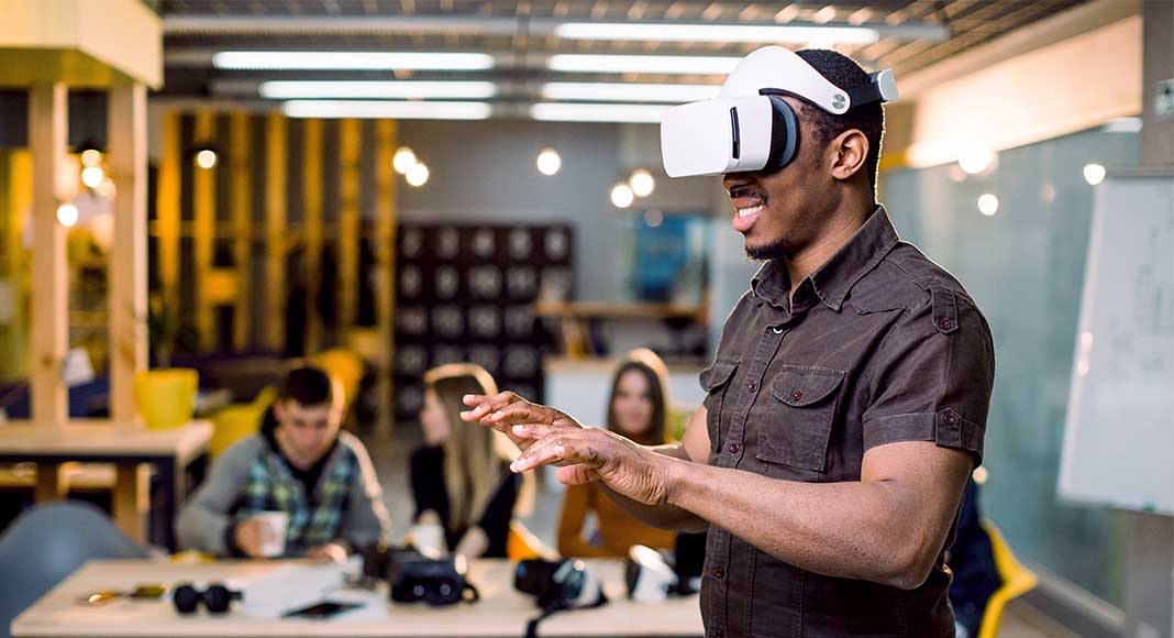 A man wearing a virtual reality headset stands before colleagues in an office space
