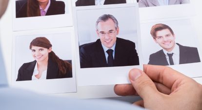 Headshot photos of several business people with a hand holding one of them.