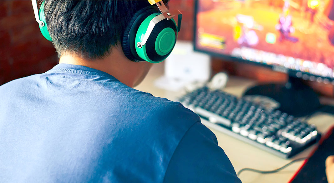 Boy wearing headphones facing computer screen with video game