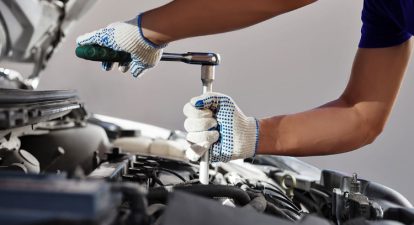 A mechanic using a socket wrench under the hood of a car, representing a selection of automotive commercial sample scripts.