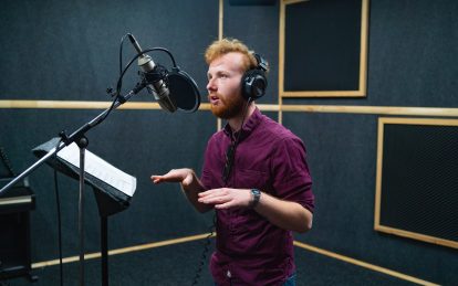 Expressive bearded man with curly ginger hair in headphones at recording studio