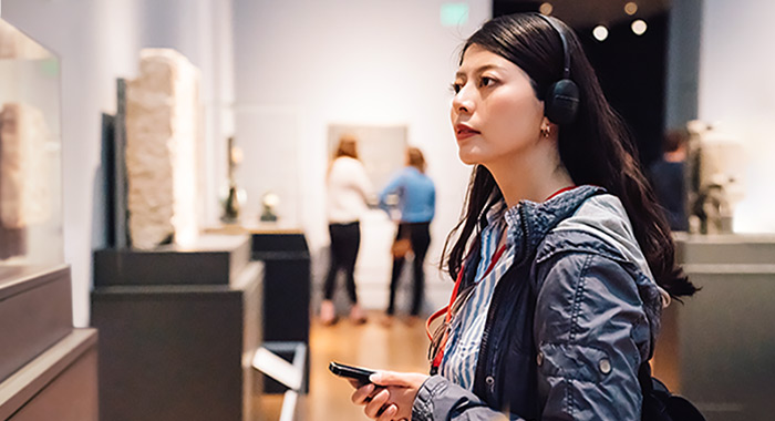 Dark-haired woman listening to audio recording generated from text to speech software at a museum