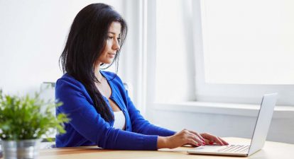 Woman with dark hair sitting and using laptop