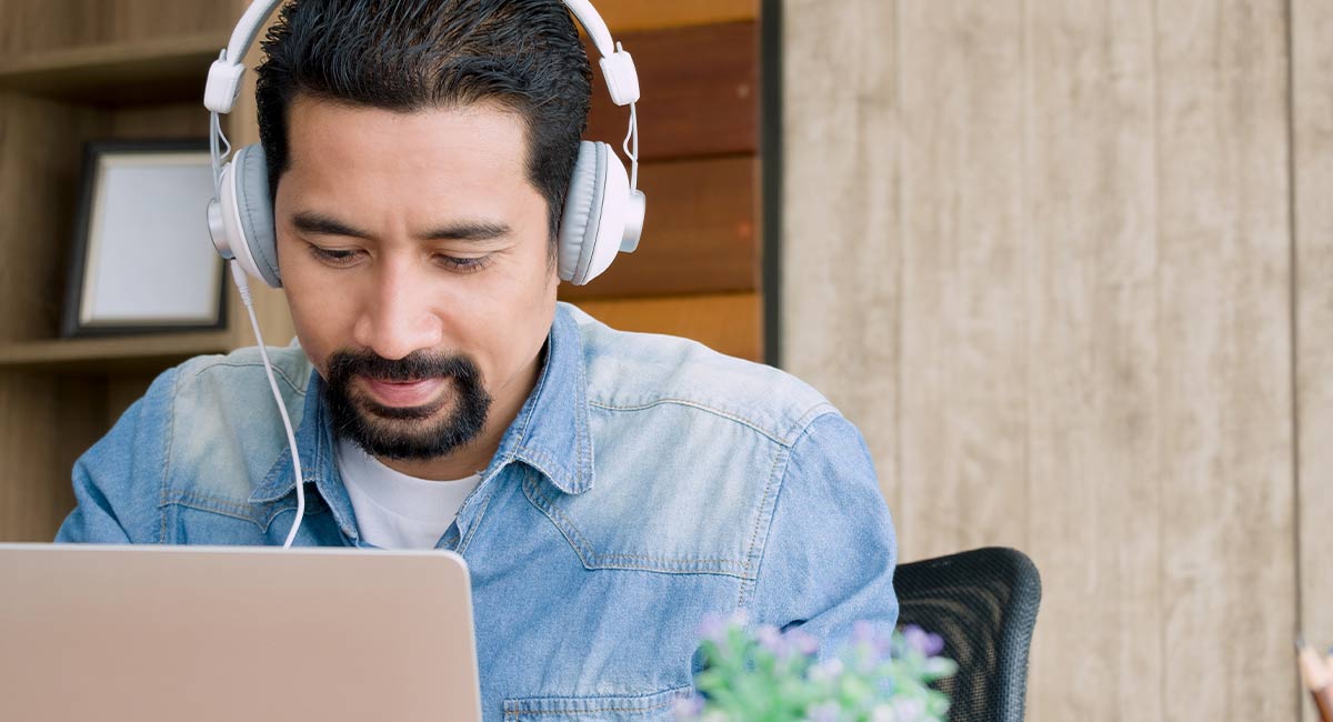 man sitting at a laptop with silver headphones on. Image for a blog post on the top 5 sound effect websites