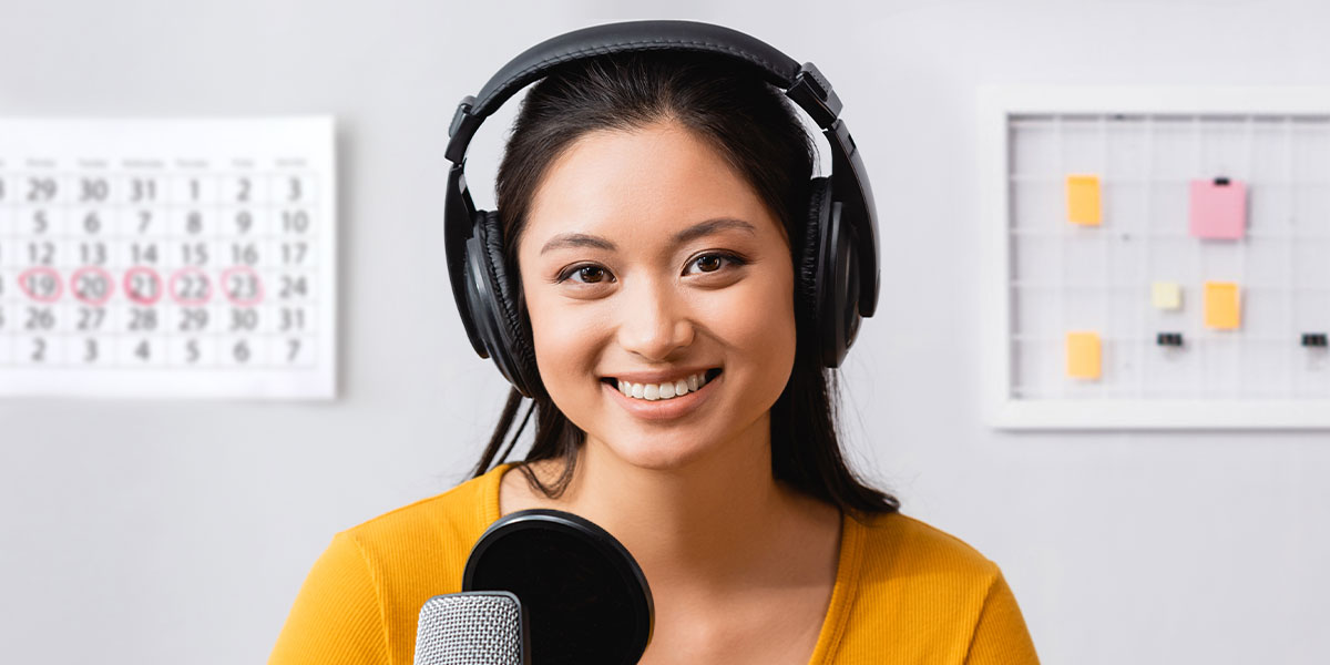 Female voice actor wearing headphones while recording her voice at microphone equipped with pop filter