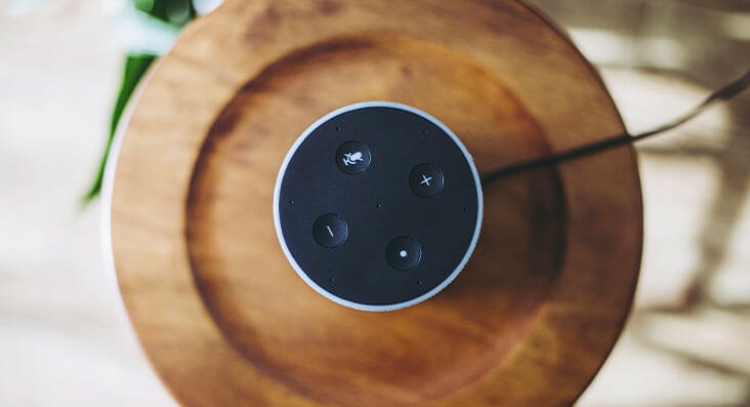 A black smart home speaker sitting on a brown circular piece of wood.