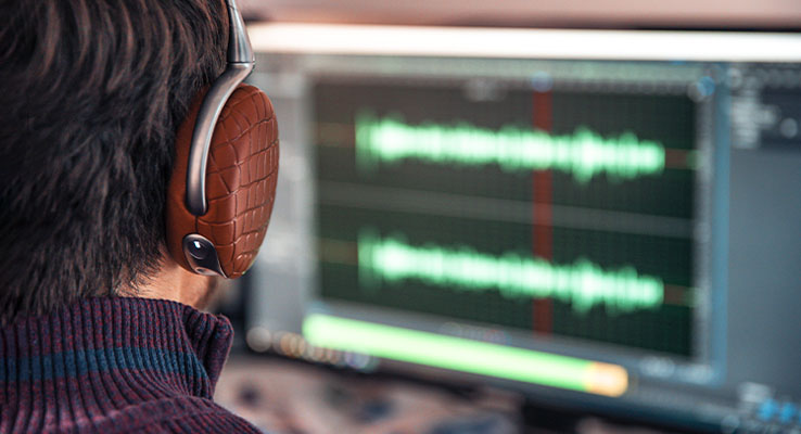person wearing red headphones sitting in front of a computer editing audio.