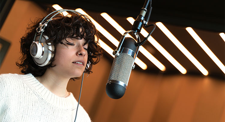 woman standing in front of microphone, in a recording studio