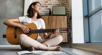 Woman sitting on floor and playing the guitar.