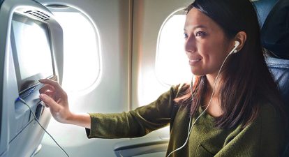 An asian woman wearing a green shirt touches the screen display in her airplane seat.