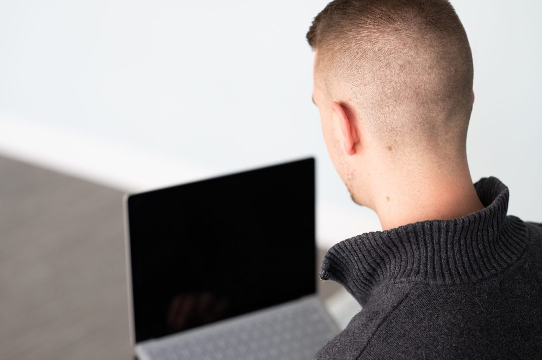 A man looking at a computer, wearing a black shirt.