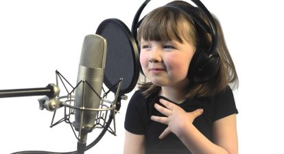 A child voice actor, a little girl around 4 years old sits in front of a microphone with headphones on.