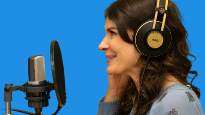 A brunette woman wearing headphones speaks into a microphone in front of a blue background.