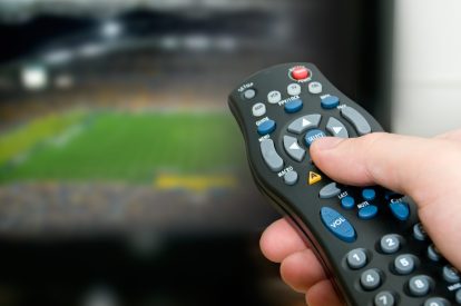 A hand holding a remote and pointing it towards a color television.