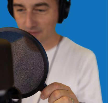 A man wearing a white shirt adjusts a pop filter in front of his microphone.