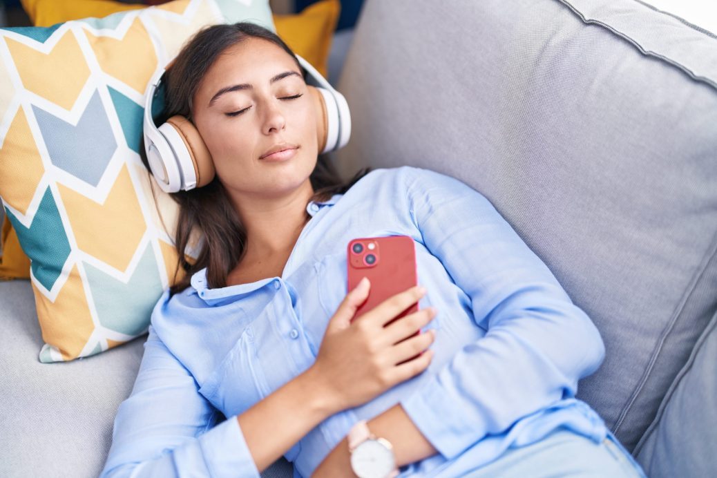 Young hispanic woman listening to music sleeping on sofa at home