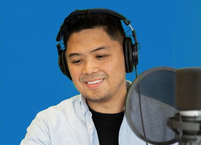 A Filipino man looks at his phone while he sits in front of a microphone.