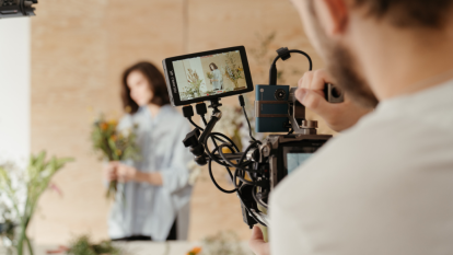A man with a commercial video camera films a woman holds a bouquet of flowers.