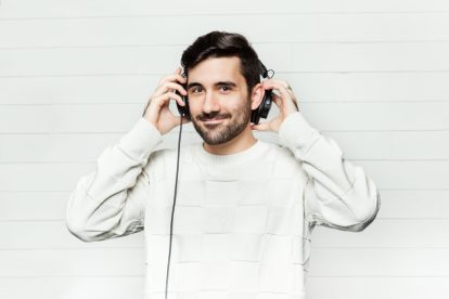 A main with black hair and a beard is wearing headphones and smiling towards the camera.