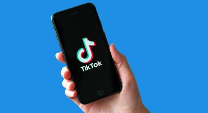 A hand holding up a phone with the TikTok logo in front of a blue background.