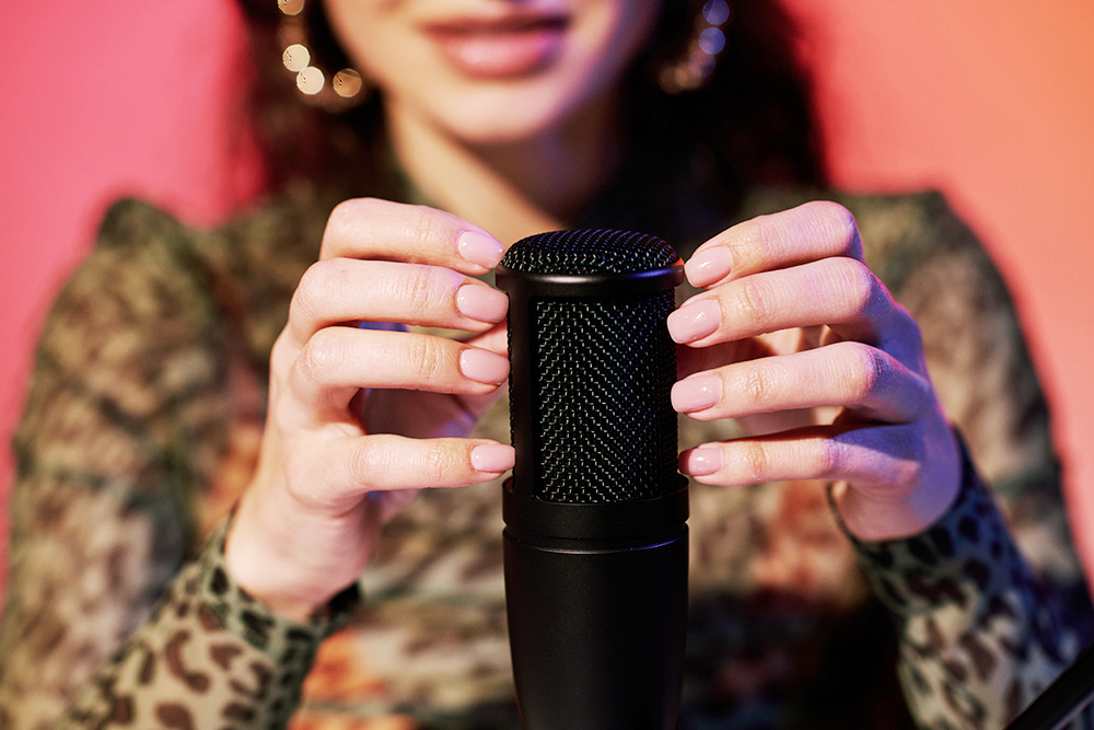 A woman taps her fingers on a microphone.