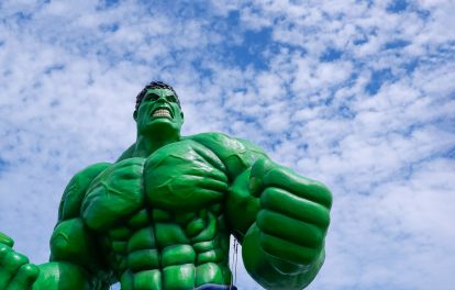 Low angle view of the large outdoor Hulk model display on roadside area against white cloudy and blue sky background