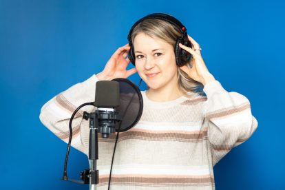 A blonde woman holds her hands against headphones on her ears.