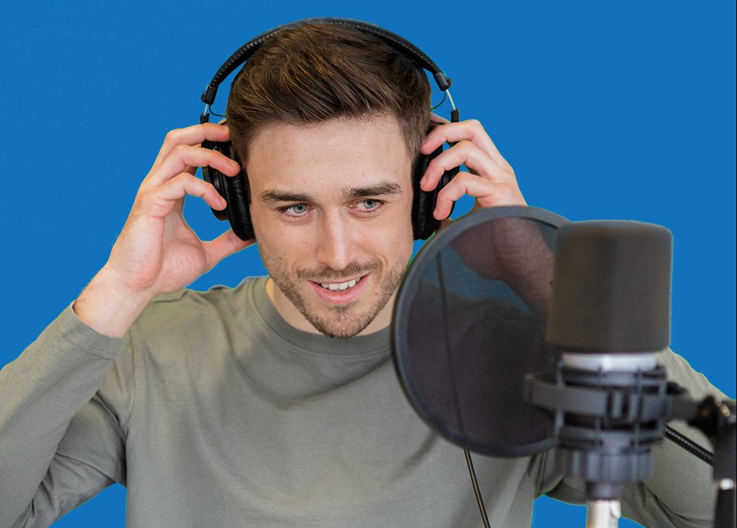 A man holding onto his headphones looking towards a microphone in a studio.