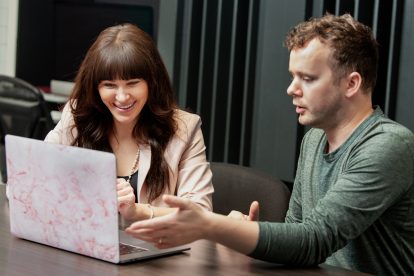 A man and a woman sit in front of a laptop in an office.