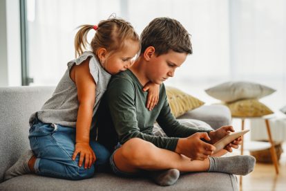 Little girl and boy watching video or playing games on their digital device tablet, smartphone. Children digital addiction concept.