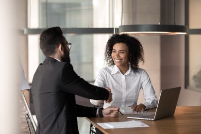 Smiling man and a woman in an office shaking hands over a deal