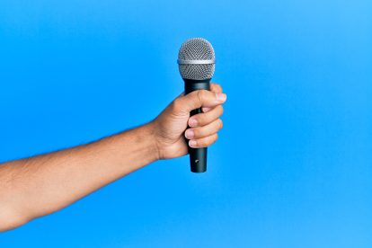 A man's hand holding a microphone against a sky blue background.