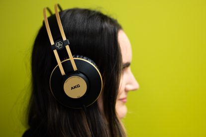 The side profile of a woman with long brown hair wearing headphones and standing against a lime-colored wall