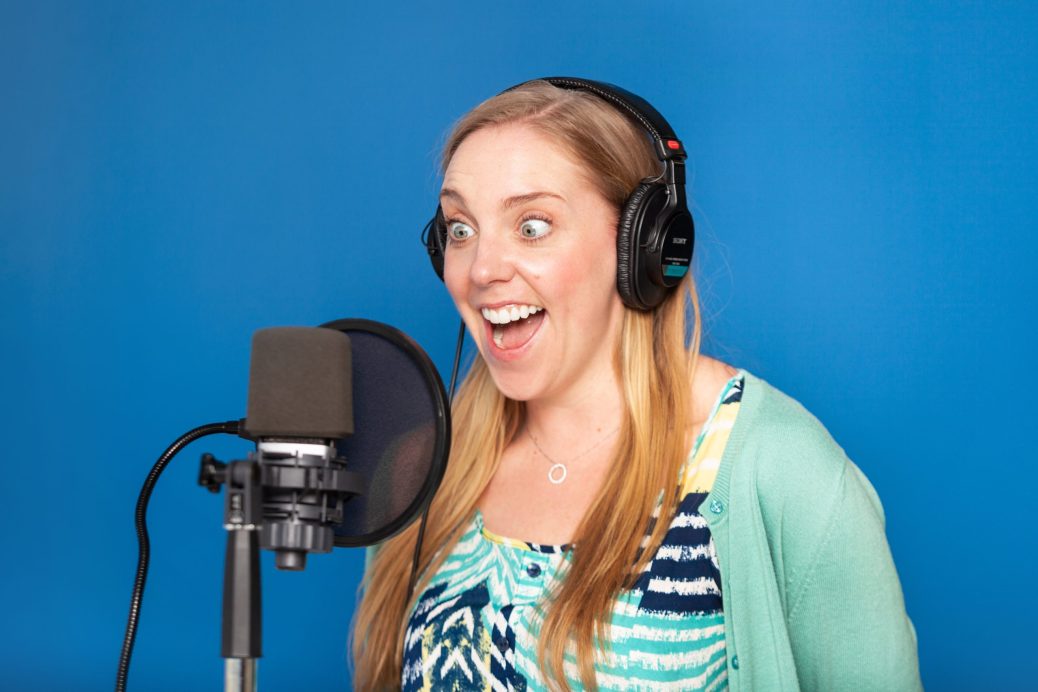 A woman singing into a microphone against a blue background