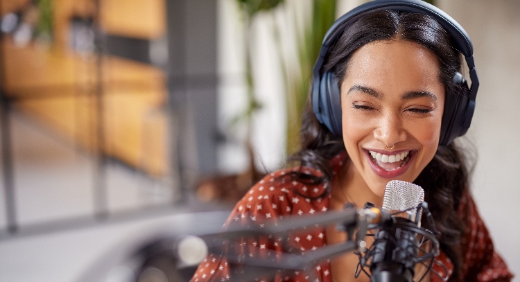 Cheerful young woman with a microphone recording audio and video content in studio.