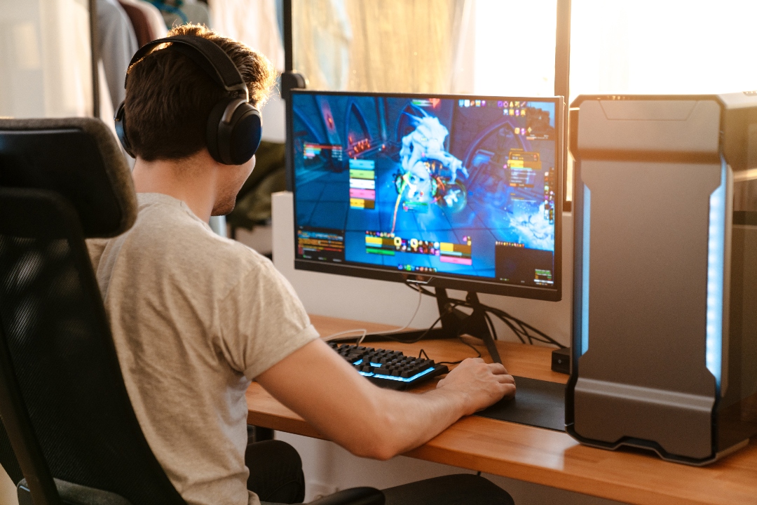 A man wears headphones and sits at his computer playing video games.