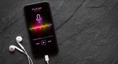 A smartphone with the word podcast and a microphone icon in purple on the screen, representing a podcast trailer playing on a smart device.