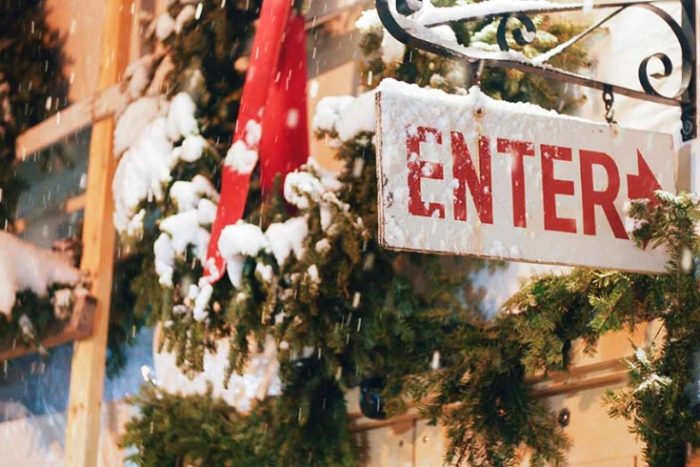 An enter sign covered in snow against a background of pine boughs.