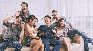 A group of friends sit on a couch, laughing as confetti rains down