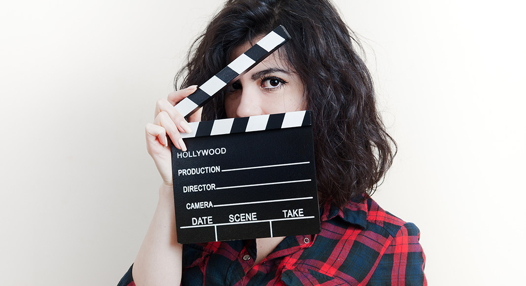 A woman holds a clapper half open as she looks at the camera
