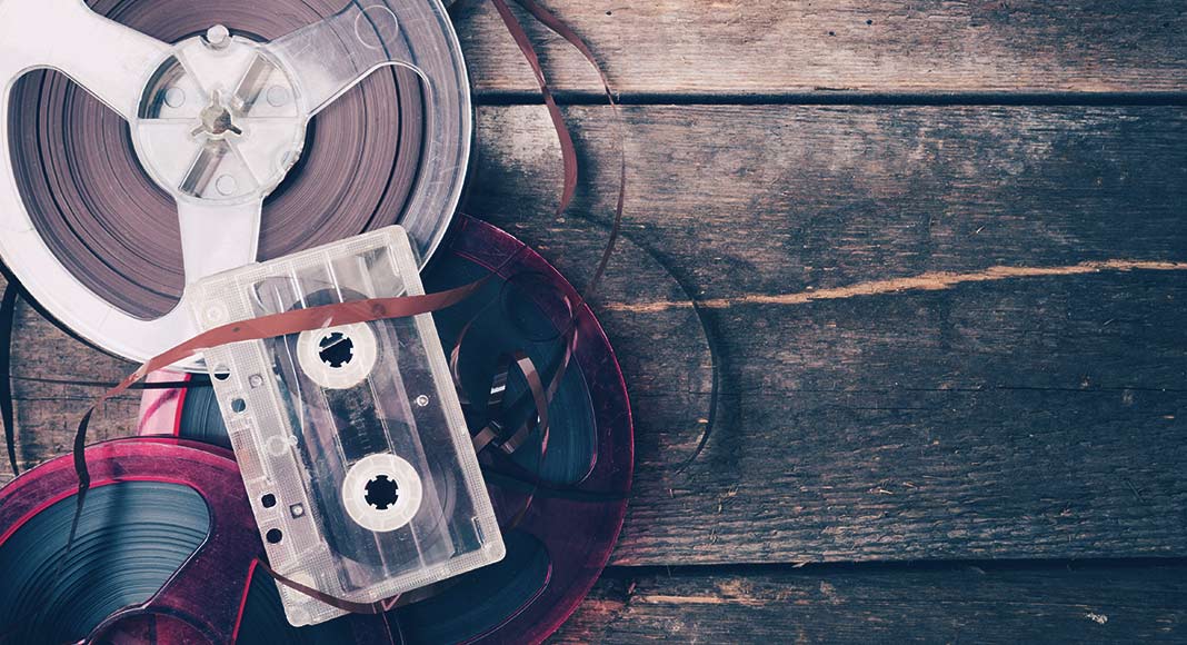 A reel of tape and a cassette sit on a wooden floor