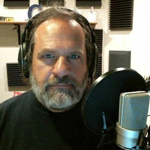 Tommy Griffiths sits in front of a microphone with a pop filter. He is wearing headphones.