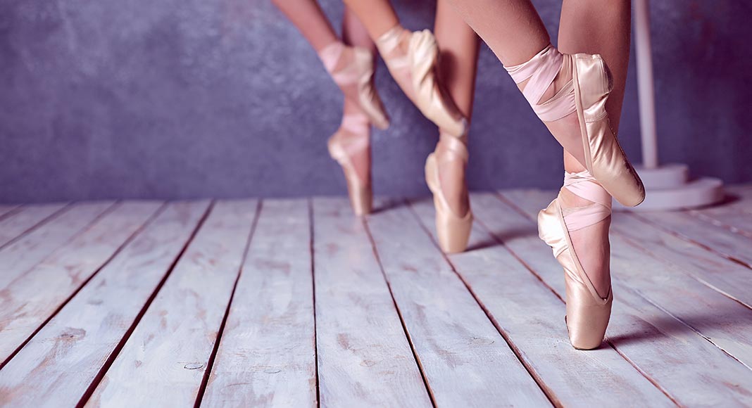 close up on the feet of three ballet dancers standing eleve