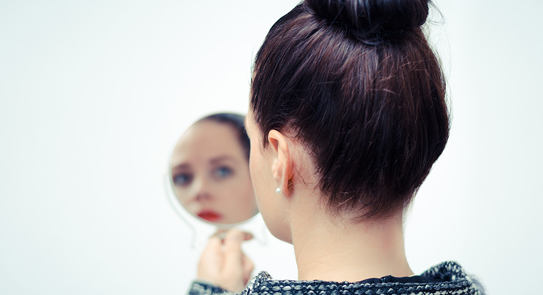 Woman holding a hand mirror and looking at her reflection.